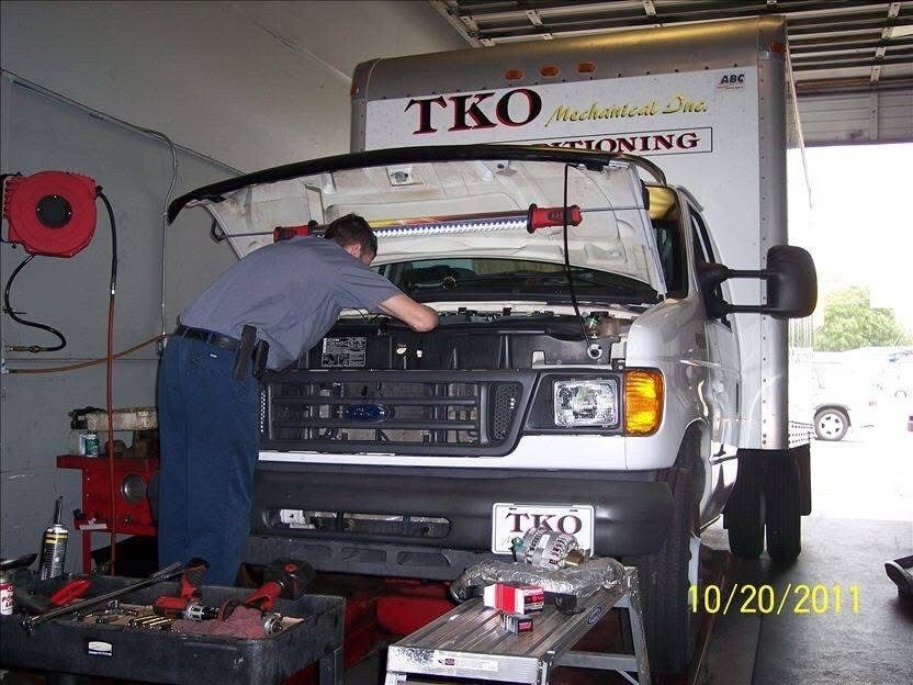 Technician performing engine diagnostics on a commercial box truck inside an auto repair shop with the hood open and tools nearby